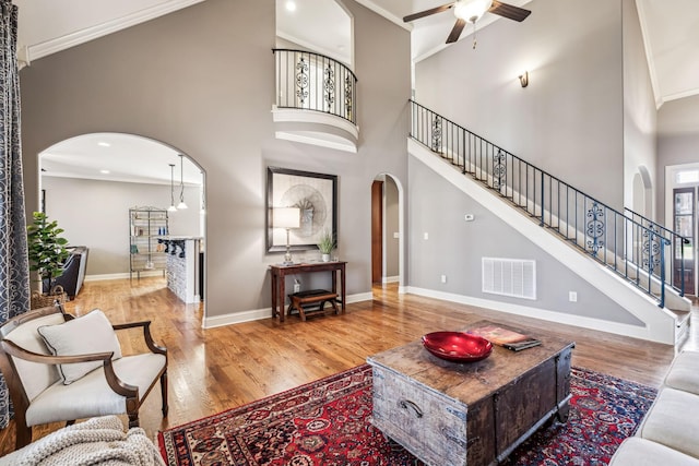 living room with hardwood / wood-style flooring, ceiling fan, ornamental molding, and a high ceiling