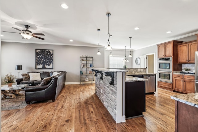 kitchen with a center island with sink, decorative light fixtures, light stone counters, and appliances with stainless steel finishes