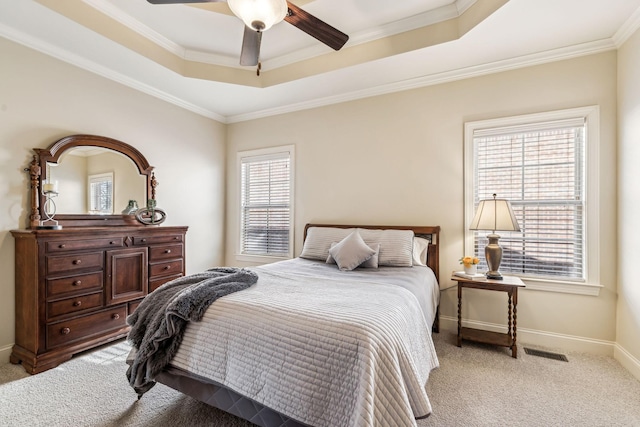 carpeted bedroom with ceiling fan, multiple windows, and a tray ceiling