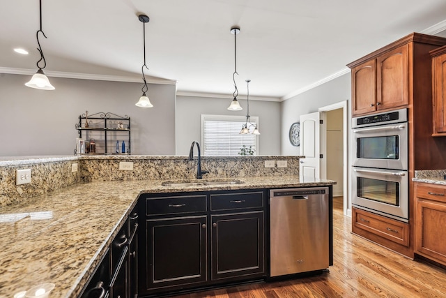 kitchen featuring pendant lighting, crown molding, sink, light stone countertops, and appliances with stainless steel finishes