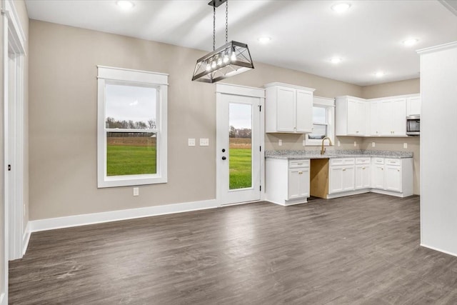 kitchen featuring white cabinetry, sink, dark wood-type flooring, hanging light fixtures, and light stone counters