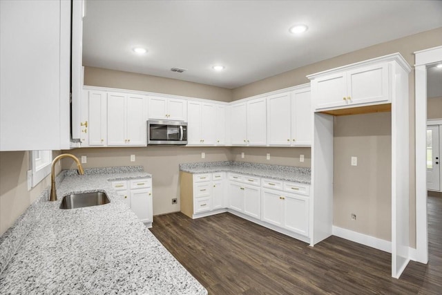 kitchen with light stone countertops, white cabinetry, dark wood-type flooring, and sink