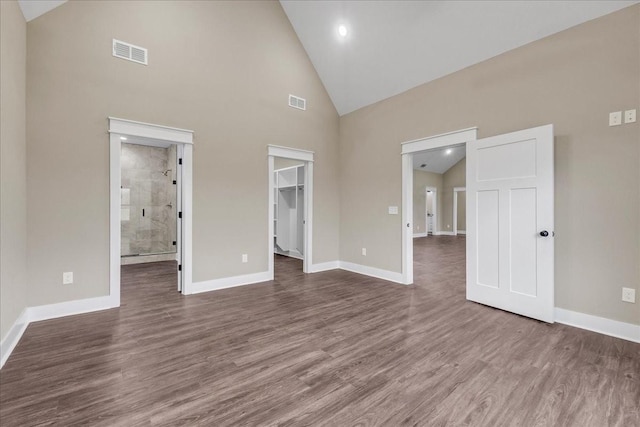 interior space with connected bathroom, high vaulted ceiling, a walk in closet, a closet, and hardwood / wood-style flooring