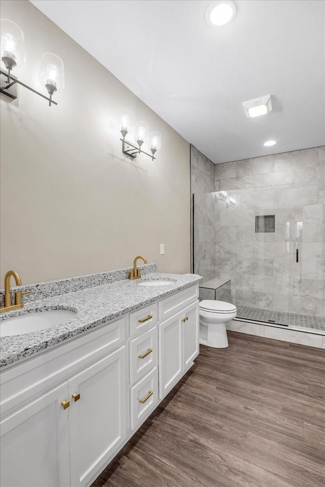 bathroom with tiled shower, vanity, hardwood / wood-style flooring, and toilet