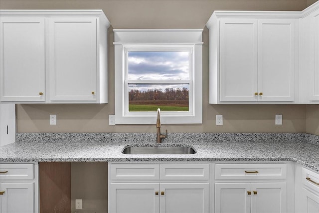 kitchen featuring light stone counters, sink, and white cabinets