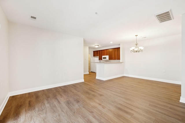 unfurnished living room with a notable chandelier and light wood-type flooring