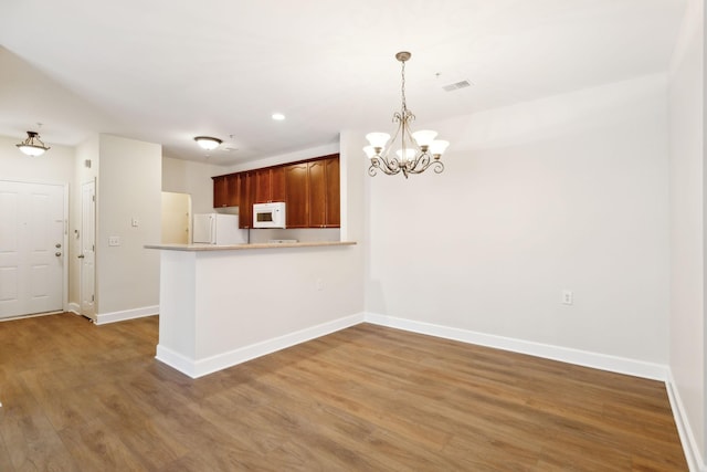 kitchen featuring kitchen peninsula, white appliances, decorative light fixtures, a notable chandelier, and dark hardwood / wood-style floors