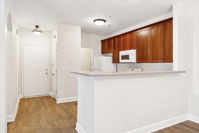 kitchen featuring white appliances, kitchen peninsula, and light hardwood / wood-style flooring