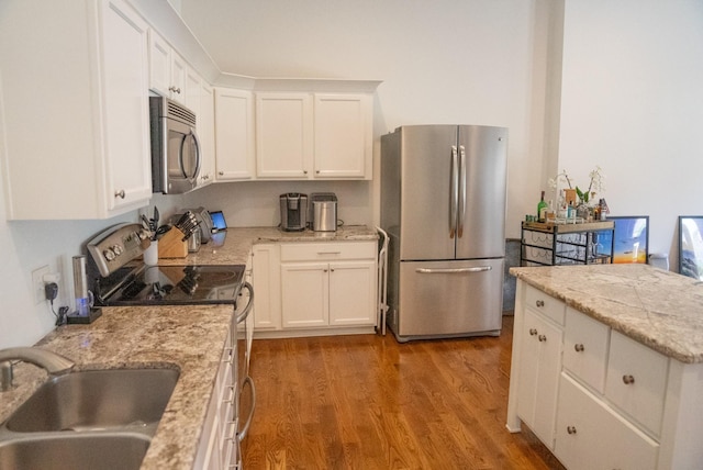 kitchen with light stone countertops, appliances with stainless steel finishes, sink, light hardwood / wood-style flooring, and white cabinets