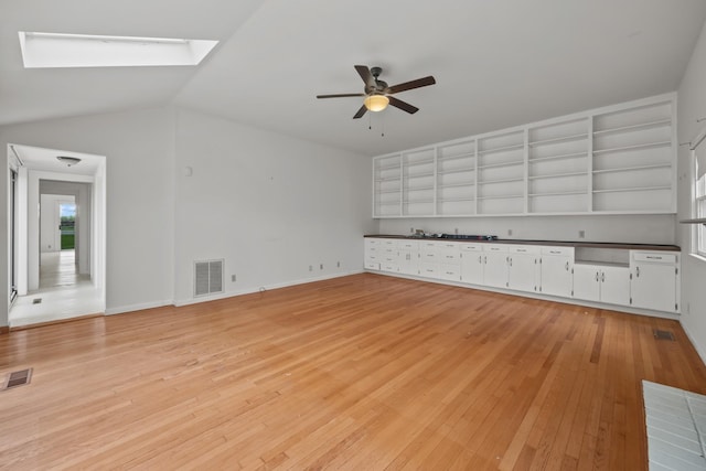 unfurnished living room featuring light wood-type flooring, ceiling fan, and vaulted ceiling with skylight