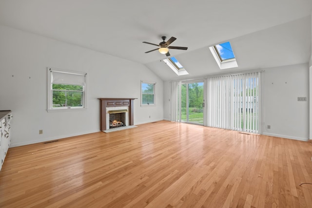 unfurnished living room featuring ceiling fan, vaulted ceiling with skylight, light hardwood / wood-style flooring, and a brick fireplace