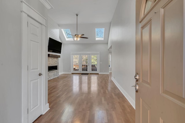 unfurnished living room featuring high vaulted ceiling, a stone fireplace, a skylight, hardwood / wood-style flooring, and ceiling fan