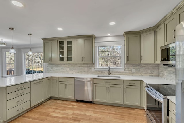 kitchen with sink, hanging light fixtures, light hardwood / wood-style floors, kitchen peninsula, and stainless steel appliances