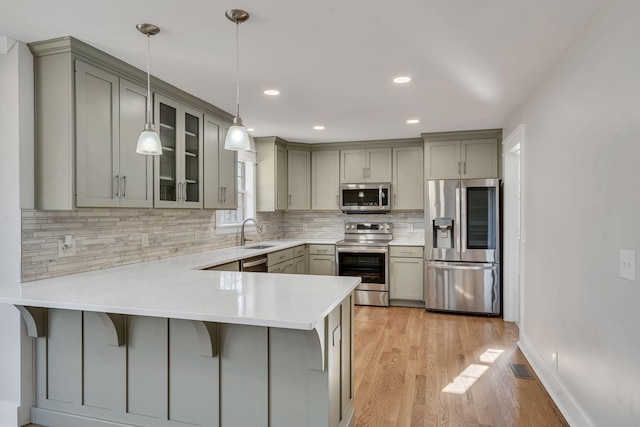 kitchen featuring kitchen peninsula, pendant lighting, gray cabinetry, and stainless steel appliances