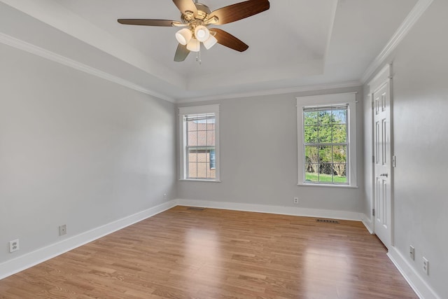 empty room featuring light wood-type flooring, a tray ceiling, ceiling fan, and crown molding