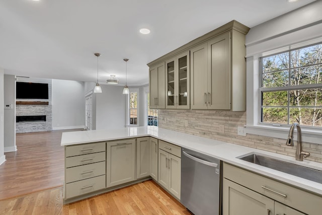 kitchen with dishwasher, sink, a stone fireplace, kitchen peninsula, and pendant lighting