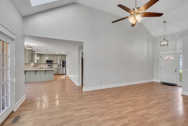 unfurnished living room with ceiling fan with notable chandelier, high vaulted ceiling, and light hardwood / wood-style flooring