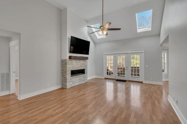 unfurnished living room featuring a skylight, ceiling fan, light hardwood / wood-style flooring, high vaulted ceiling, and a fireplace