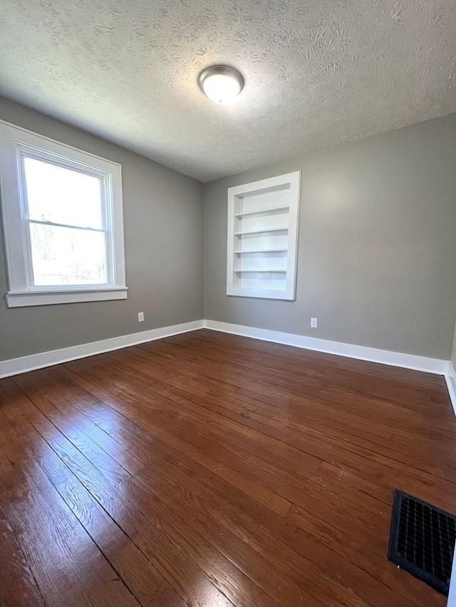 unfurnished room featuring dark hardwood / wood-style flooring, built in features, and a textured ceiling