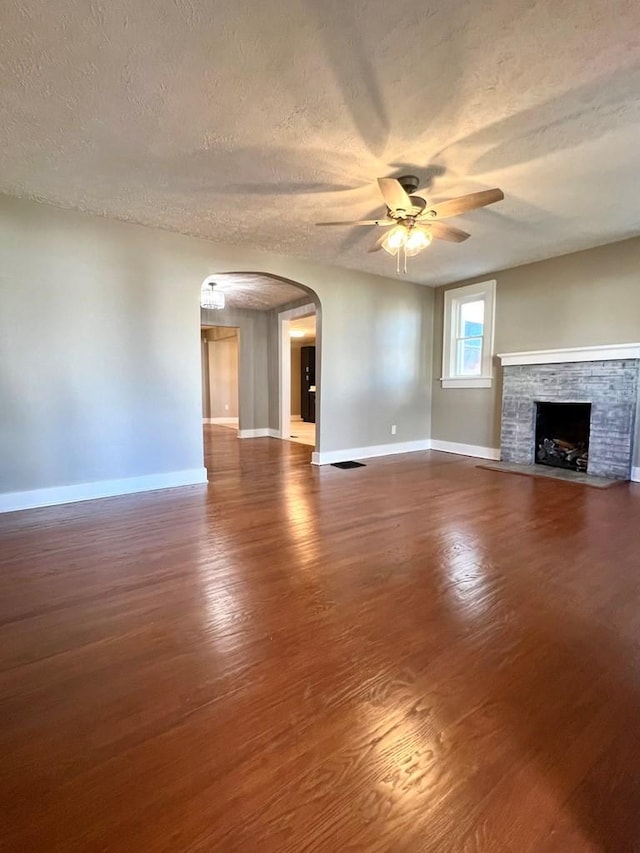 unfurnished living room with a stone fireplace, ceiling fan, wood-type flooring, and a textured ceiling