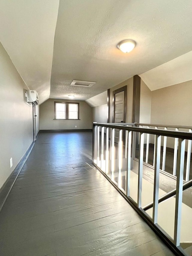 hall featuring an AC wall unit, lofted ceiling, dark hardwood / wood-style flooring, and a textured ceiling