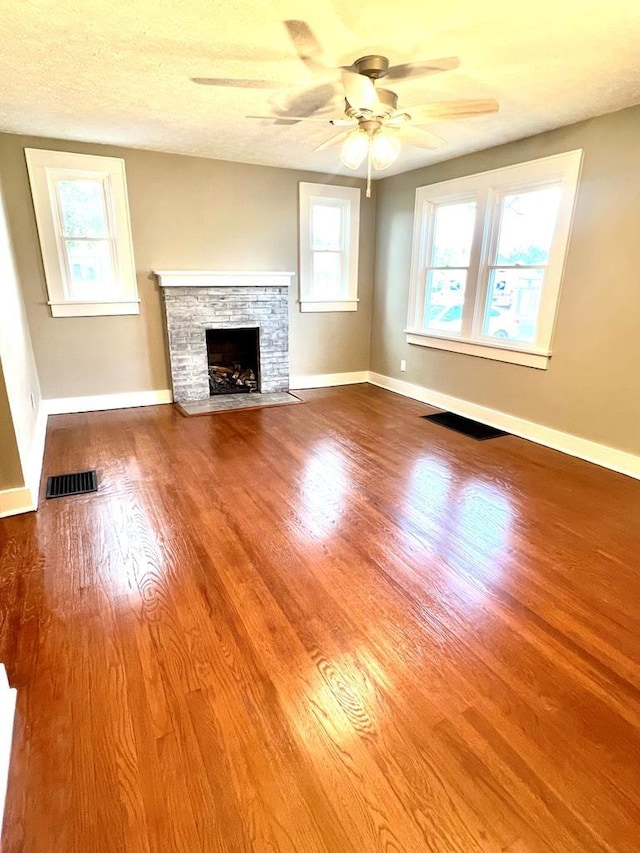 unfurnished living room with a fireplace, a textured ceiling, hardwood / wood-style flooring, and ceiling fan