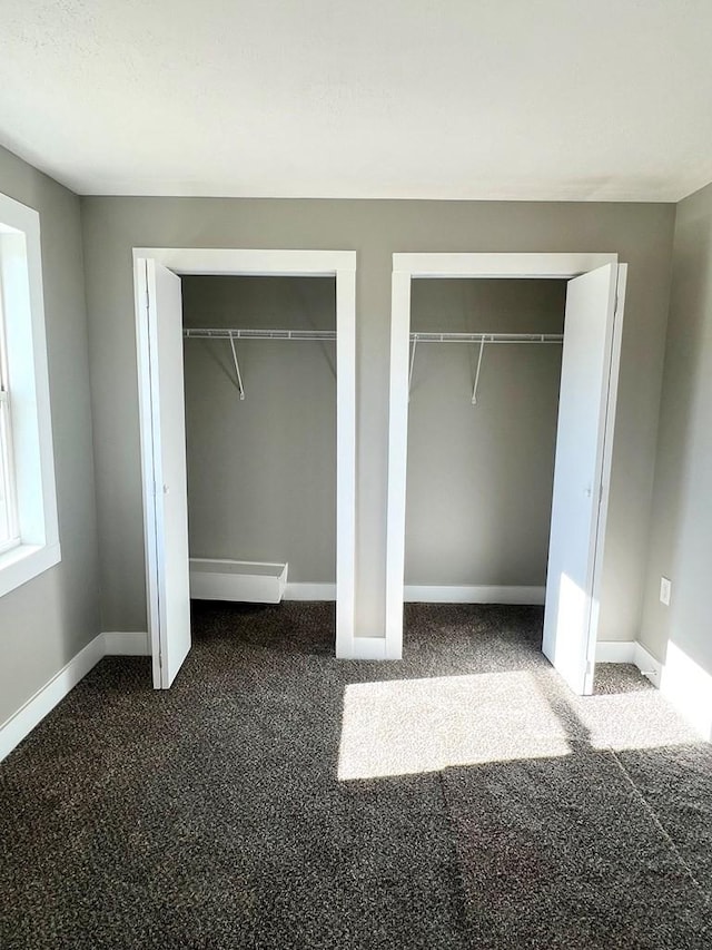 unfurnished bedroom featuring dark carpet and multiple closets