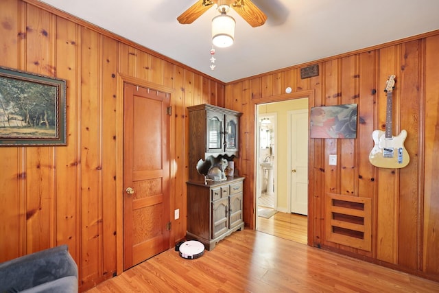 interior space featuring wooden walls, ceiling fan, light hardwood / wood-style floors, and crown molding