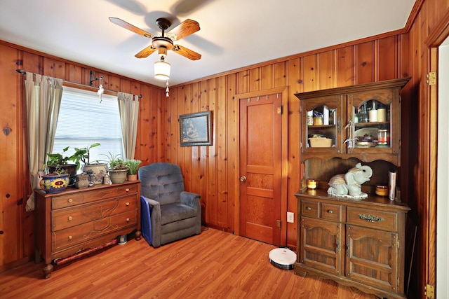 sitting room with light hardwood / wood-style floors, ceiling fan, and wooden walls