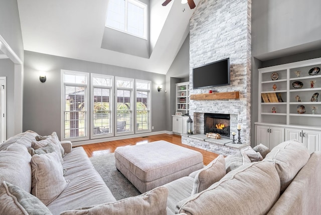 living room with high vaulted ceiling, light hardwood / wood-style flooring, ceiling fan, built in shelves, and a fireplace