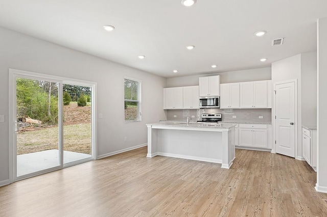 kitchen with stainless steel appliances, white cabinetry, a kitchen island with sink, and light hardwood / wood-style flooring