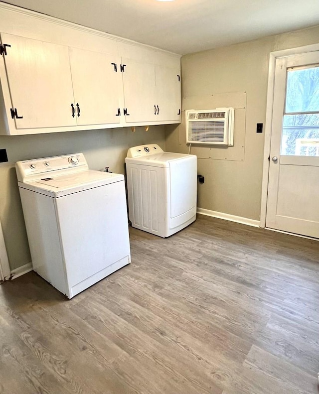 laundry area featuring a wall unit AC, washing machine and dryer, cabinets, and light hardwood / wood-style floors