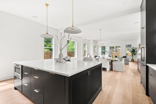 kitchen featuring pendant lighting, stainless steel microwave, a spacious island, light hardwood / wood-style flooring, and ceiling fan