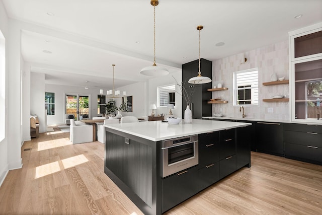 kitchen featuring light wood-type flooring, wall oven, a spacious island, sink, and hanging light fixtures