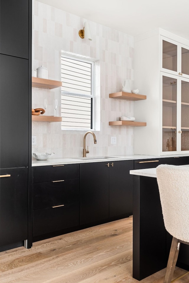 bar featuring tasteful backsplash, light hardwood / wood-style flooring, and sink