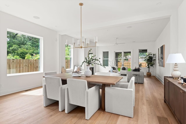 dining space with beamed ceiling, ceiling fan with notable chandelier, and light hardwood / wood-style flooring