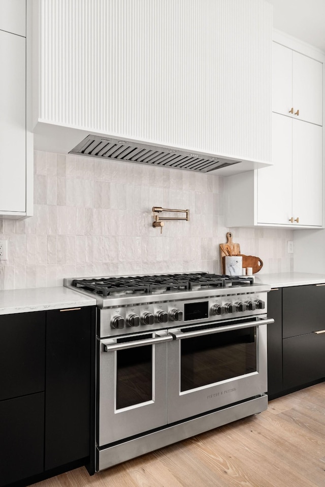 kitchen featuring tasteful backsplash, custom range hood, range with two ovens, light hardwood / wood-style flooring, and white cabinetry