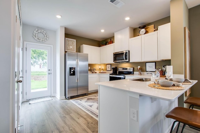 kitchen with kitchen peninsula, sink, appliances with stainless steel finishes, white cabinets, and a kitchen bar