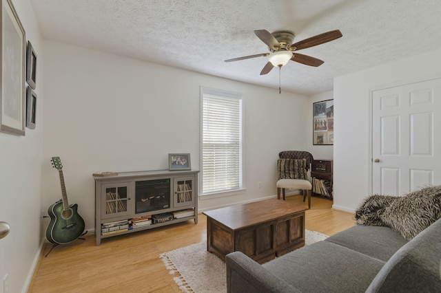 living room with ceiling fan, light hardwood / wood-style flooring, and a textured ceiling