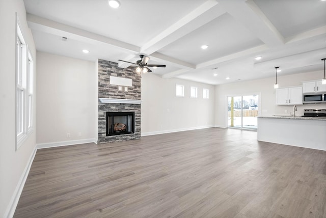 unfurnished living room with wood-type flooring, a stone fireplace, sink, and beam ceiling