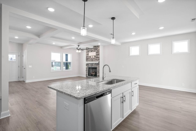 kitchen featuring sink, a stone fireplace, white cabinets, decorative light fixtures, and stainless steel dishwasher