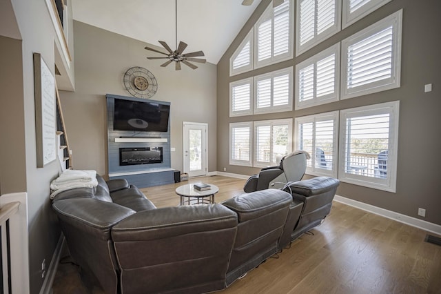 living room with ceiling fan, a high ceiling, and light wood-type flooring