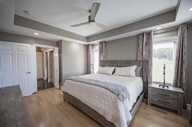 bedroom with a tray ceiling, multiple windows, ceiling fan, and light wood-type flooring