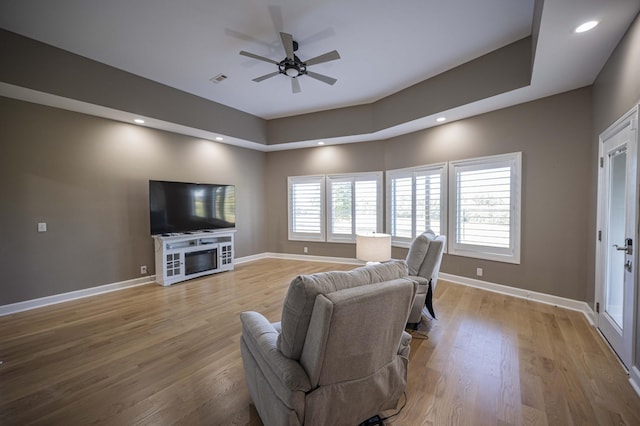 living room featuring light wood-type flooring, a raised ceiling, and ceiling fan