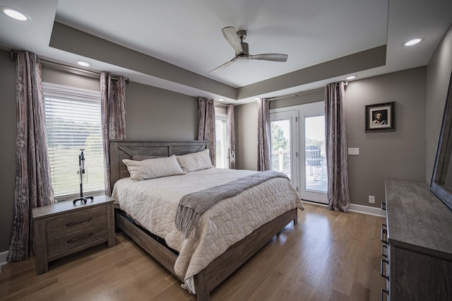 bedroom with access to exterior, light wood-type flooring, a tray ceiling, and ceiling fan