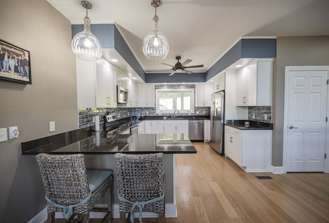 kitchen with pendant lighting, white cabinets, sink, kitchen peninsula, and stainless steel appliances