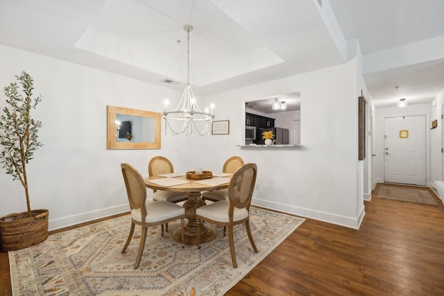 dining space featuring a chandelier, dark wood-type flooring, and a tray ceiling