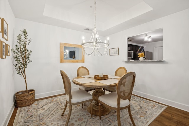 dining space featuring hardwood / wood-style flooring, a chandelier, and a tray ceiling