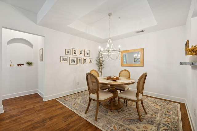 dining room with dark hardwood / wood-style flooring, a tray ceiling, and a notable chandelier