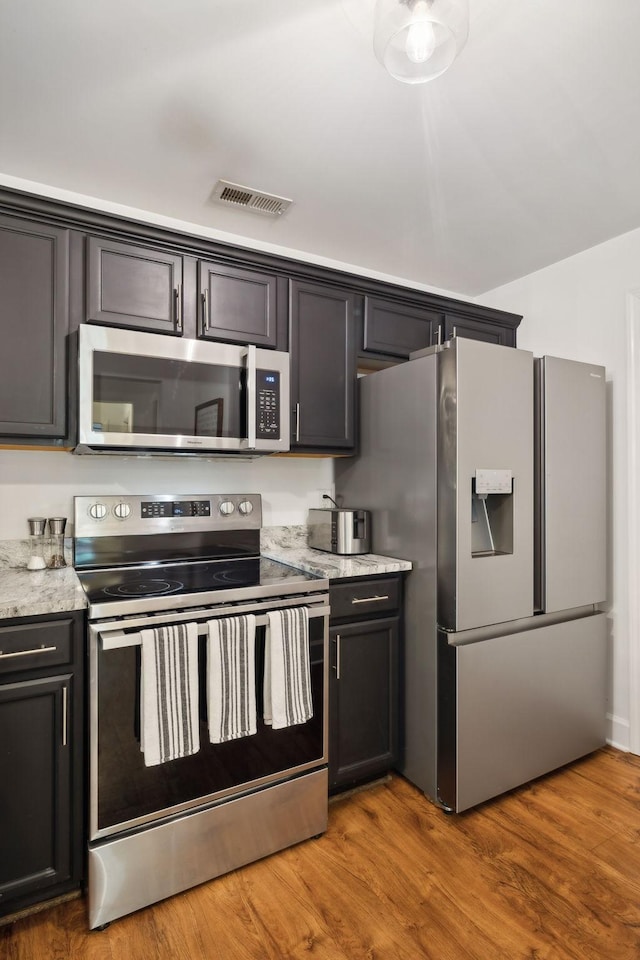 kitchen featuring light stone counters, stainless steel appliances, and hardwood / wood-style flooring